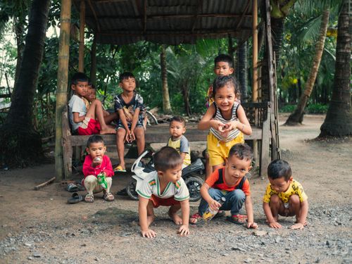 Free Group of Vietnamese children playing under a hut in a rural area, capturing joyful moments outdoors. Stock Photo
