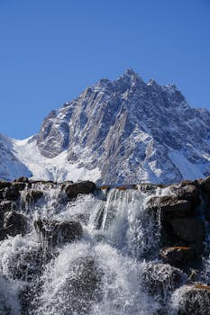 Breathtaking view of a snow-capped mountain with a cascading waterfall under a clear blue sky.