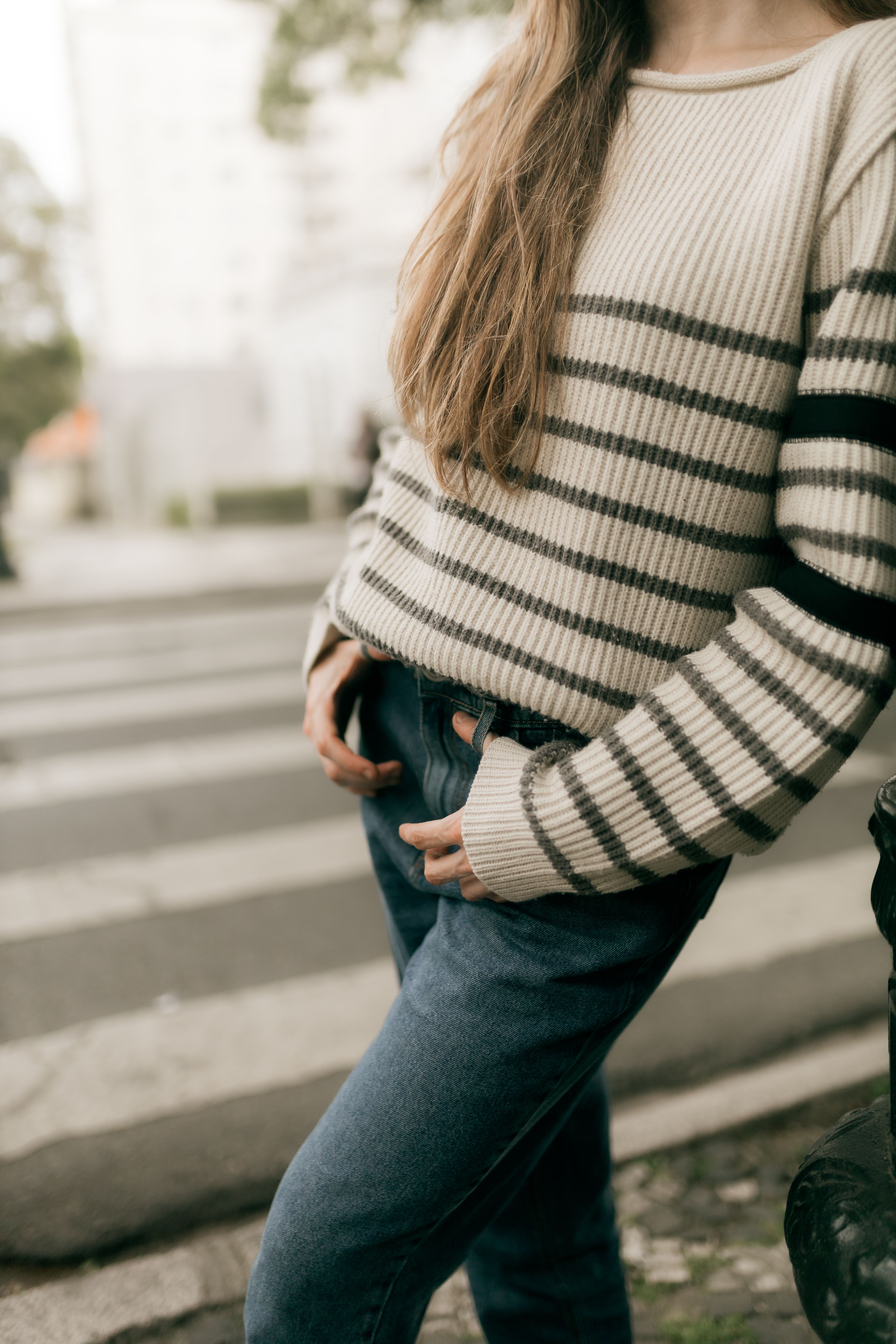 Outdoor close-up of person in striped sweater and jeans on street.