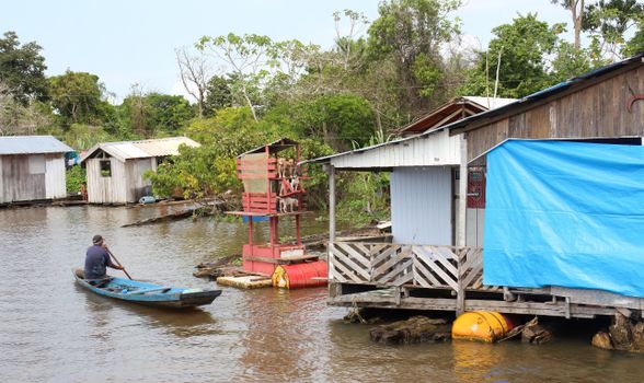 A man paddles a canoe by wooden houses on a river in Manaus, Brazil.
