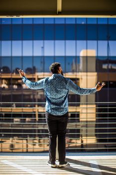 Man standing on balcony with arms open, reflecting city skyline.