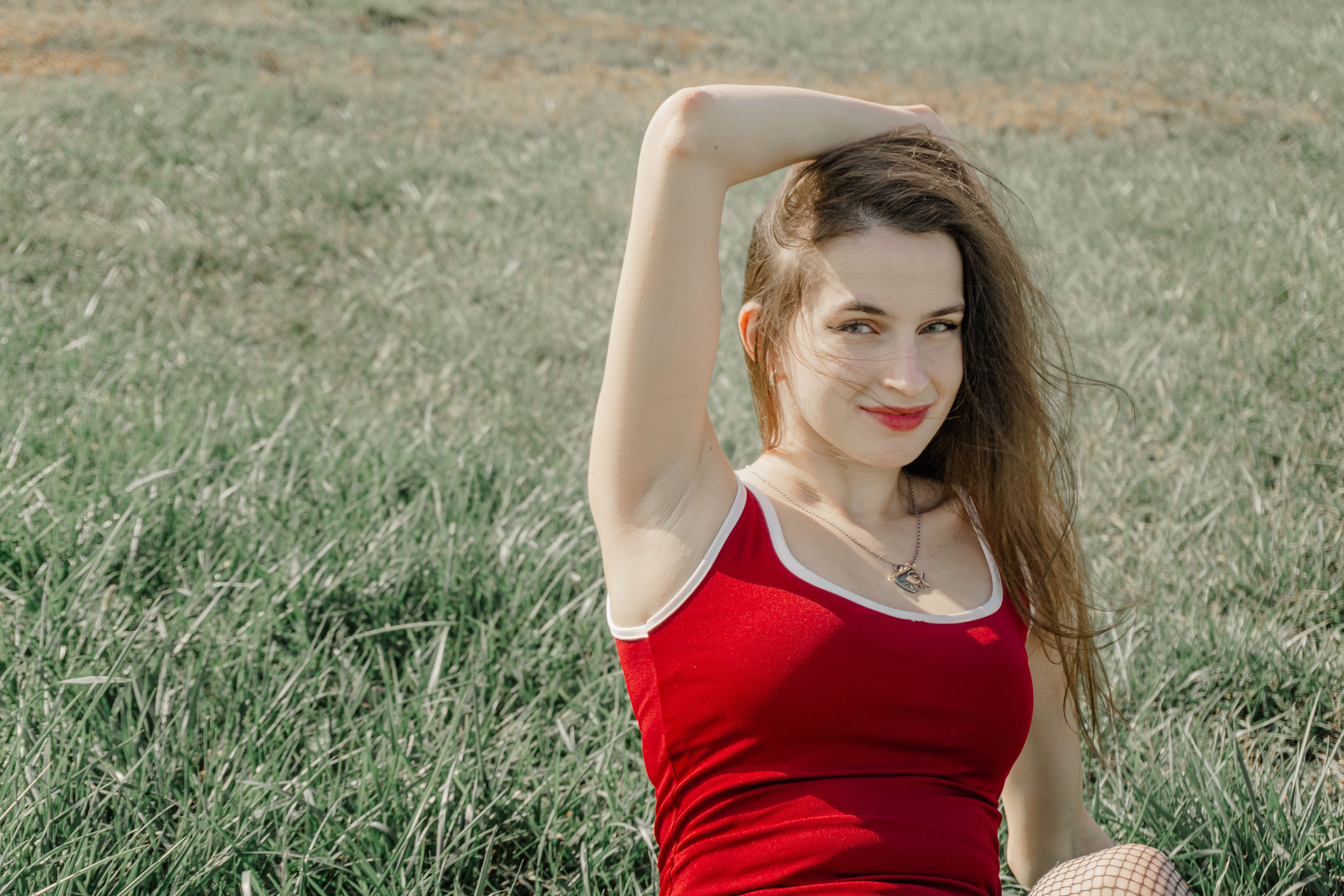 A woman in a red top posing confidently while sitting on grass with a relaxed expression.