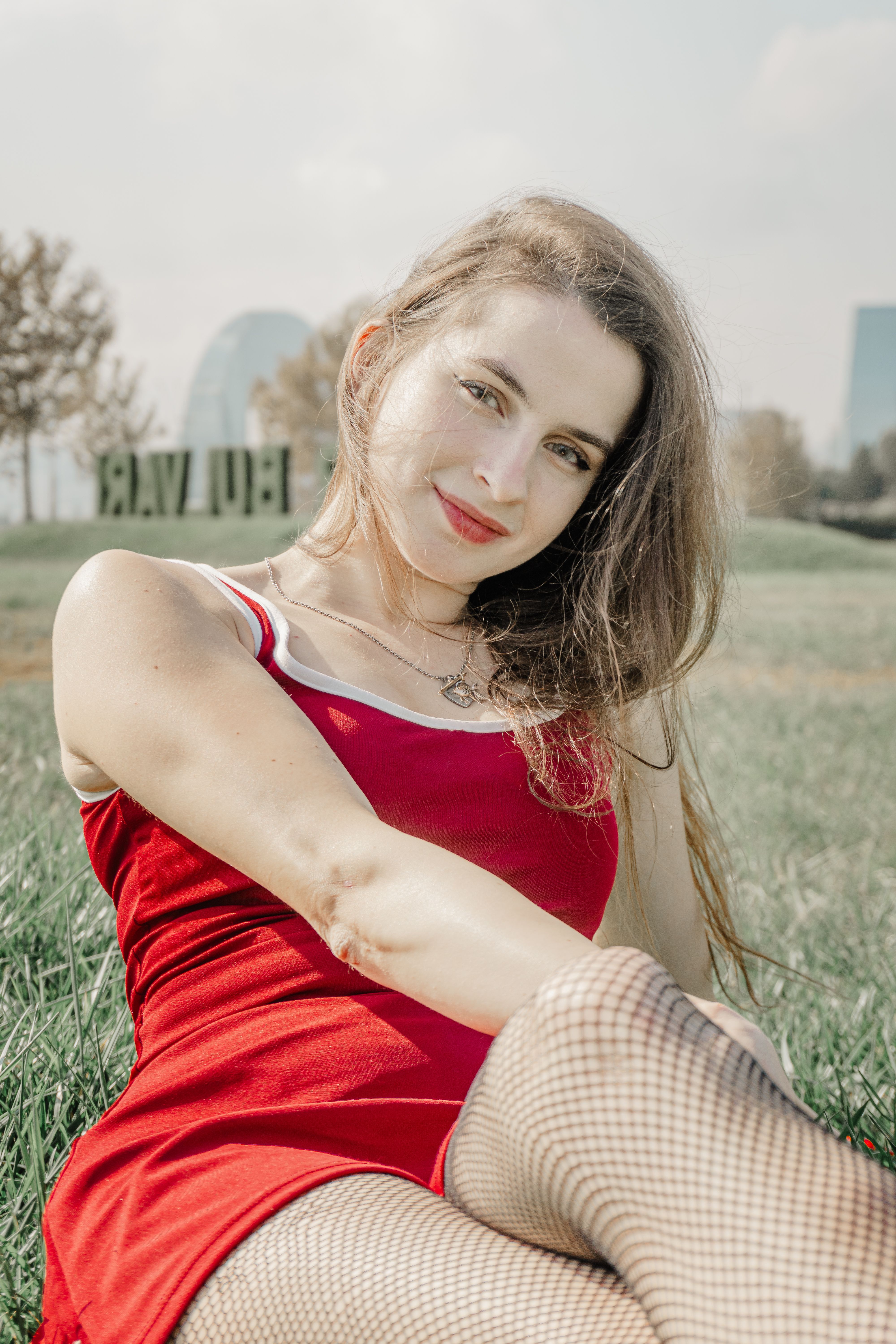 Smiling woman in a red dress enjoying a sunny day in a city park, capturing a serene outdoor vibe.