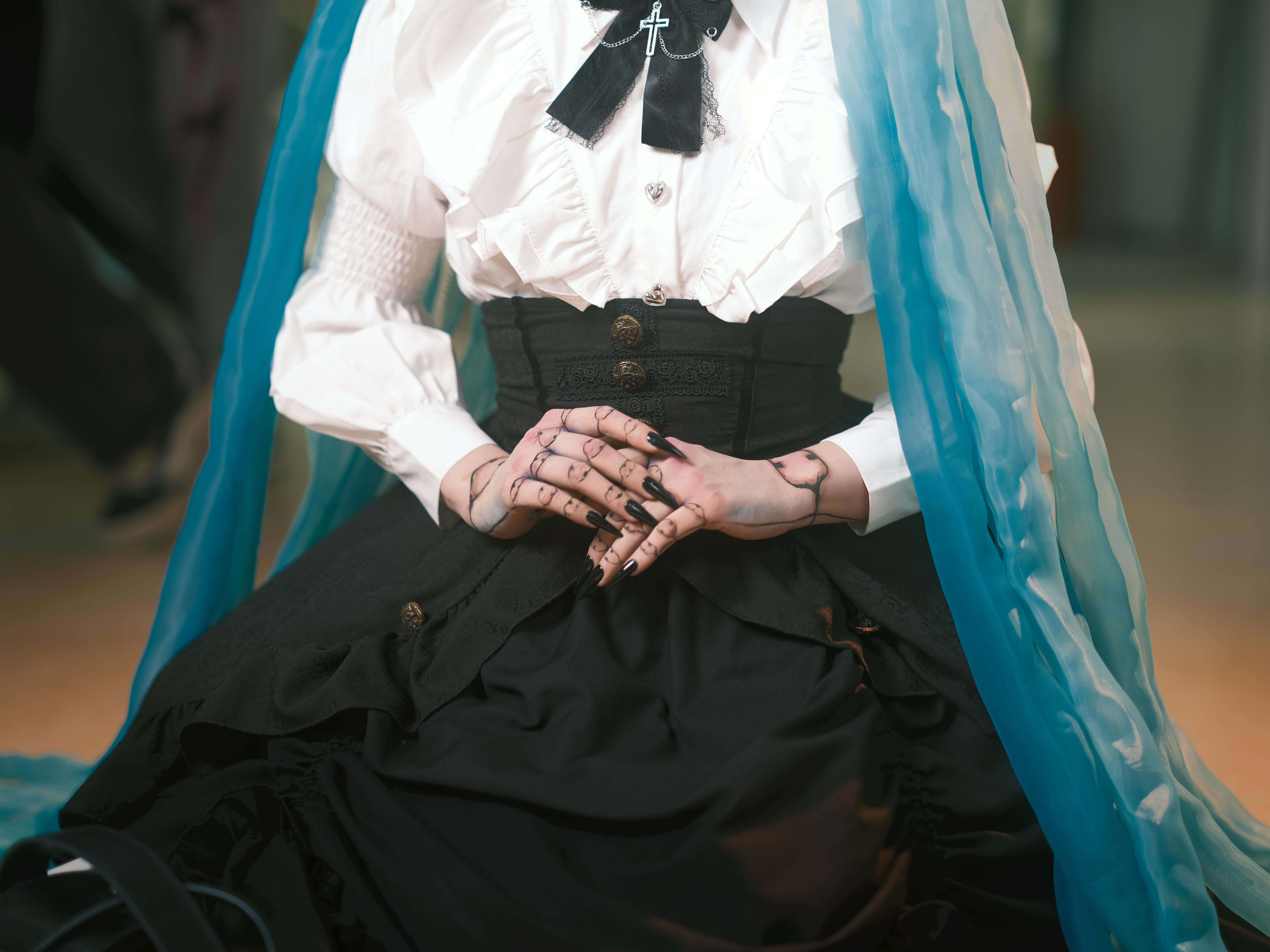 Close-up of a Gothic Lolita style outfit with a blue veil, featuring intricate hand tattoos.