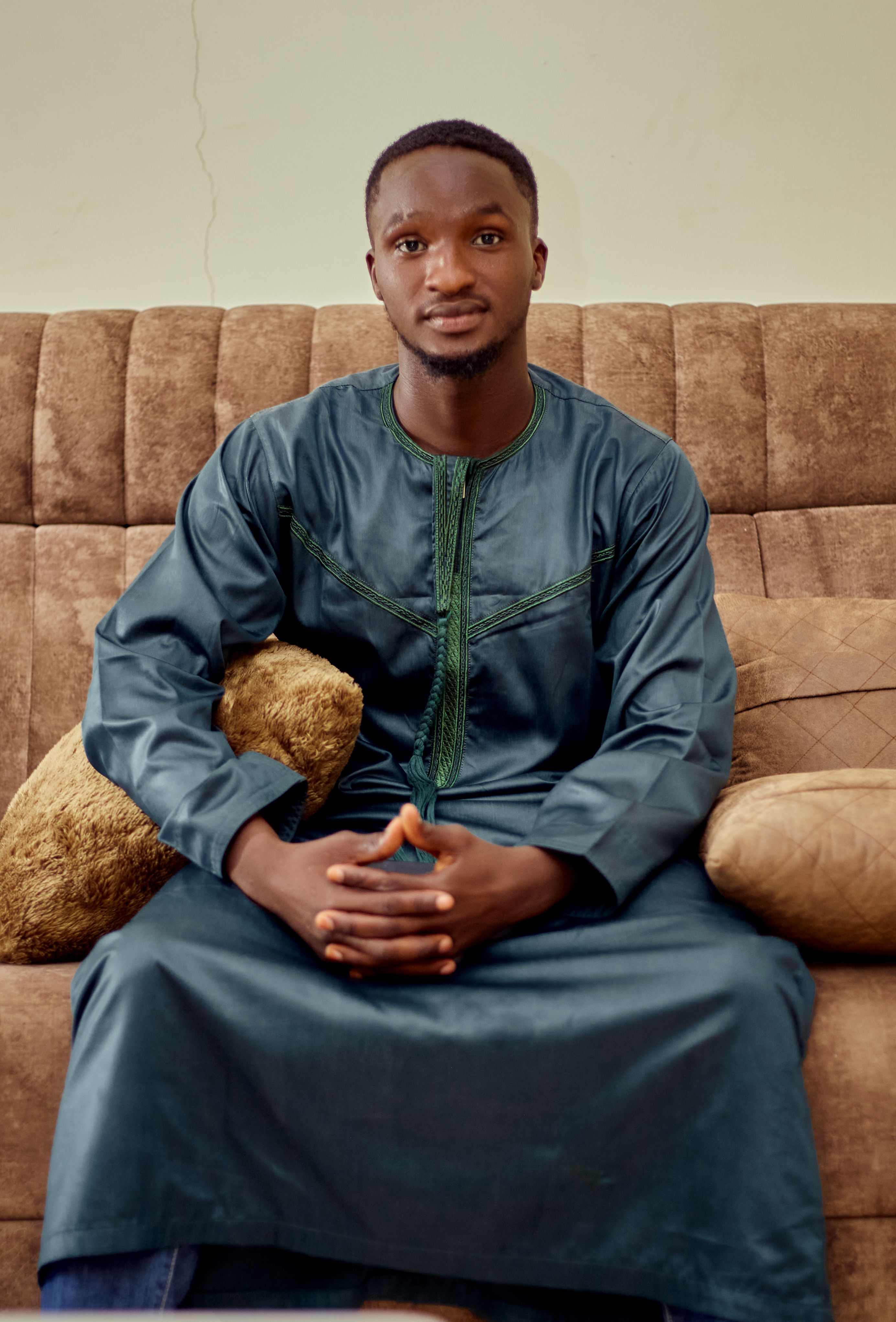 Young man sitting on a couch in traditional African attire, looking confident.