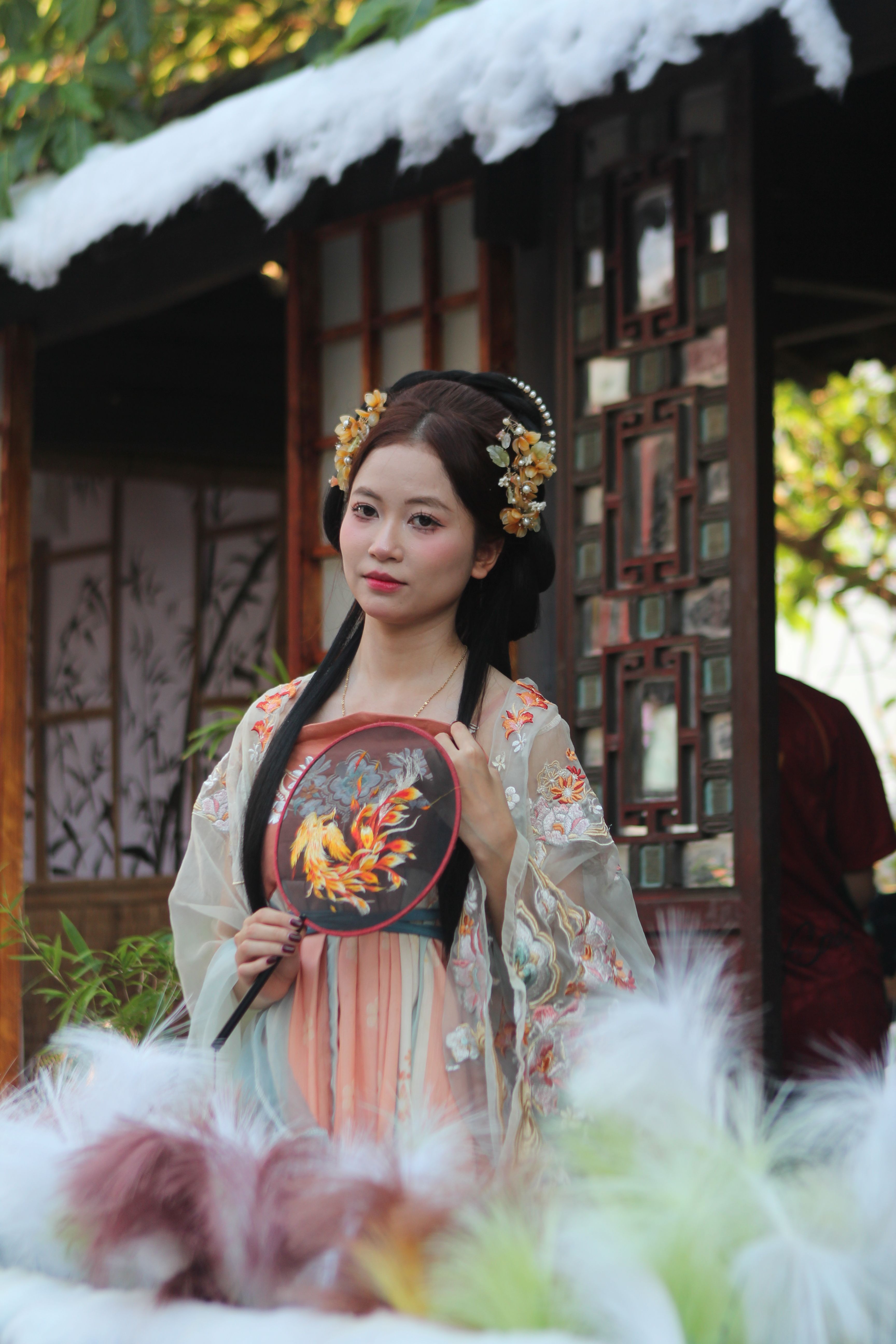 Woman in traditional Asian attire holding a decorative fan outdoors.