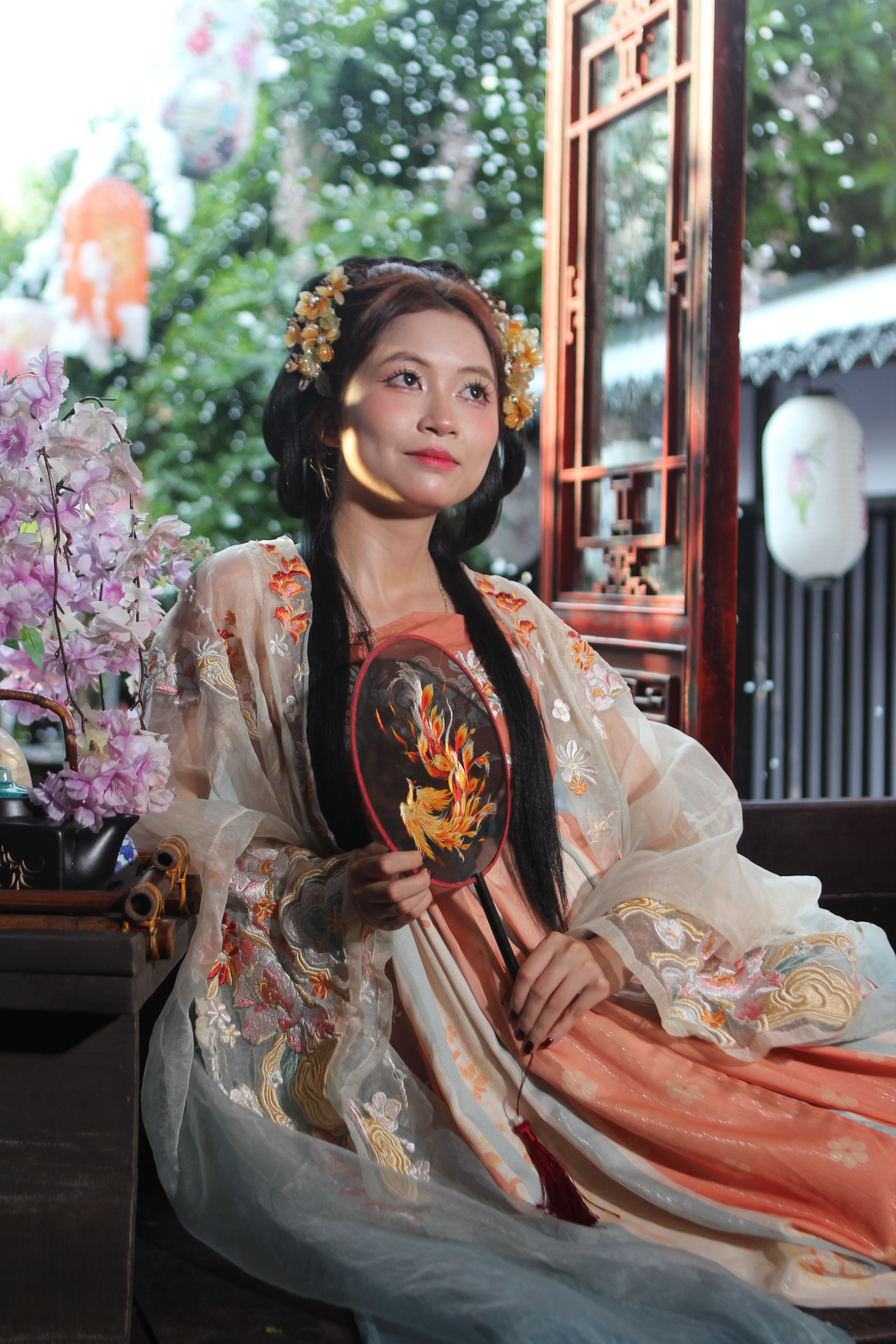 Captured in elegance, a woman in traditional Asian attire holds a decorative fan indoors.