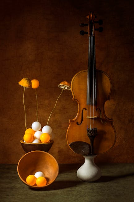 Creative still life featuring a violin and ping pong balls with warm tones and dramatic lighting.