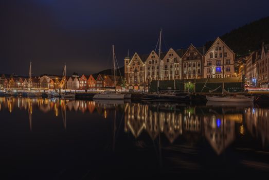 View of the illuminated Bryggen Wharf in Bergen, Norway at night, reflecting in the calm water.
