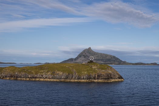 A serene coastal view featuring a grassy island and a distant mountain under a clear sky.