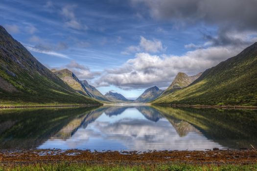 Stunning view of mountains reflected in a calm lake under a bright blue sky.