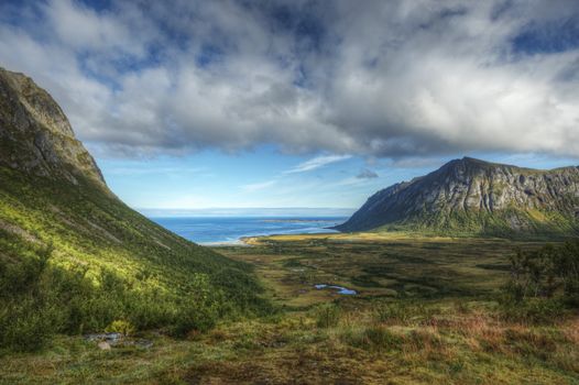 Stunning view of a lush mountain valley leading to a distant ocean under dramatic clouds.