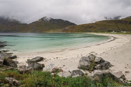 Free Tranquil beach scene with clear water and mountains under cloudy sky. Stock Photo