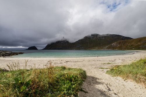 Free A serene coastal beach with mountains and dramatic clouds in the background, perfect for nature photography. Stock Photo