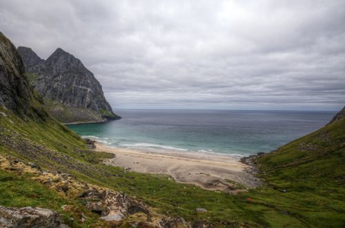 Free A stunning aerial view of a secluded beach surrounded by dramatic cliffs and green landscapes, under a cloudy sky. Stock Photo