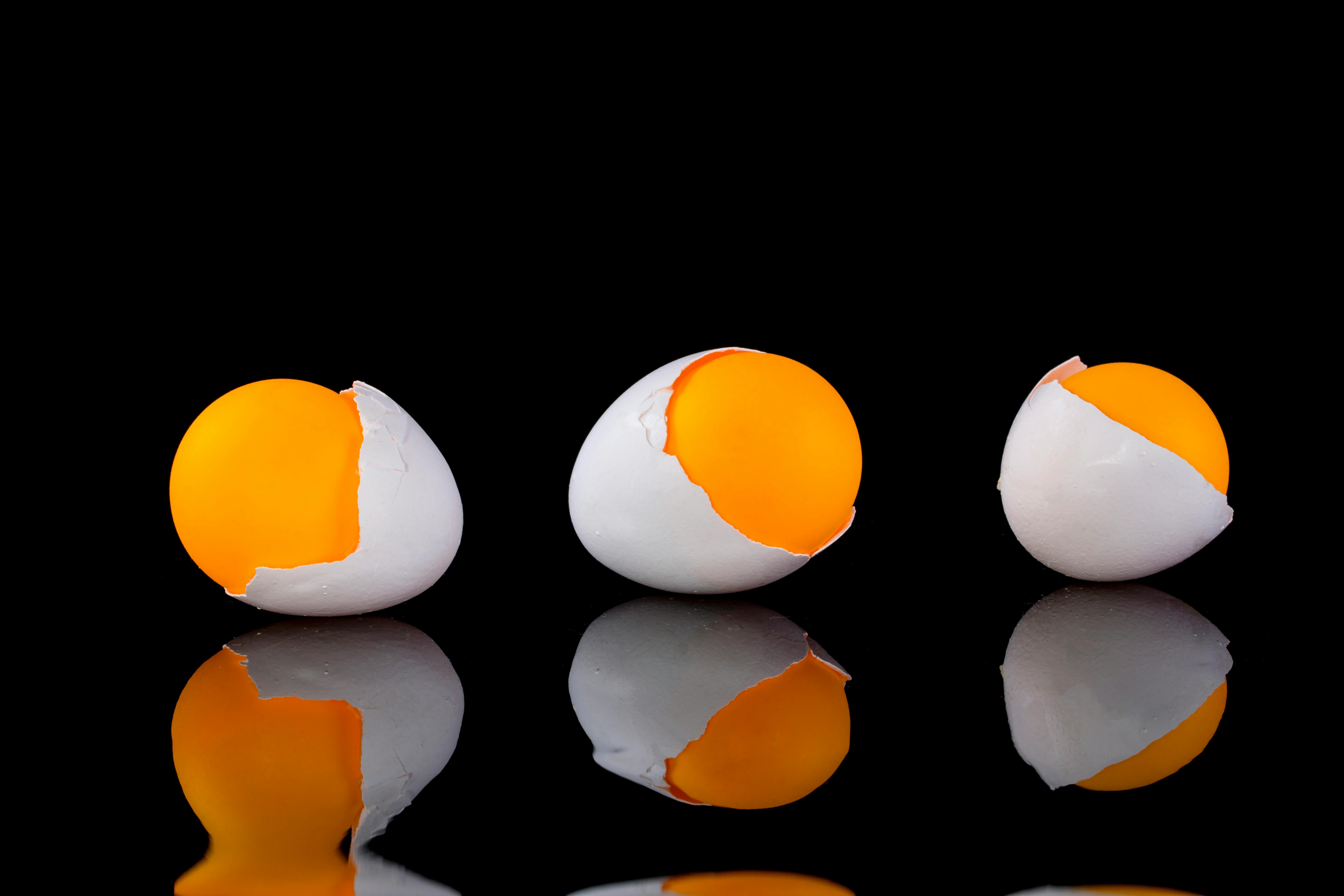 Free Three cracked egg yolks on a black reflective surface create a minimalist food concept. Stock Photo