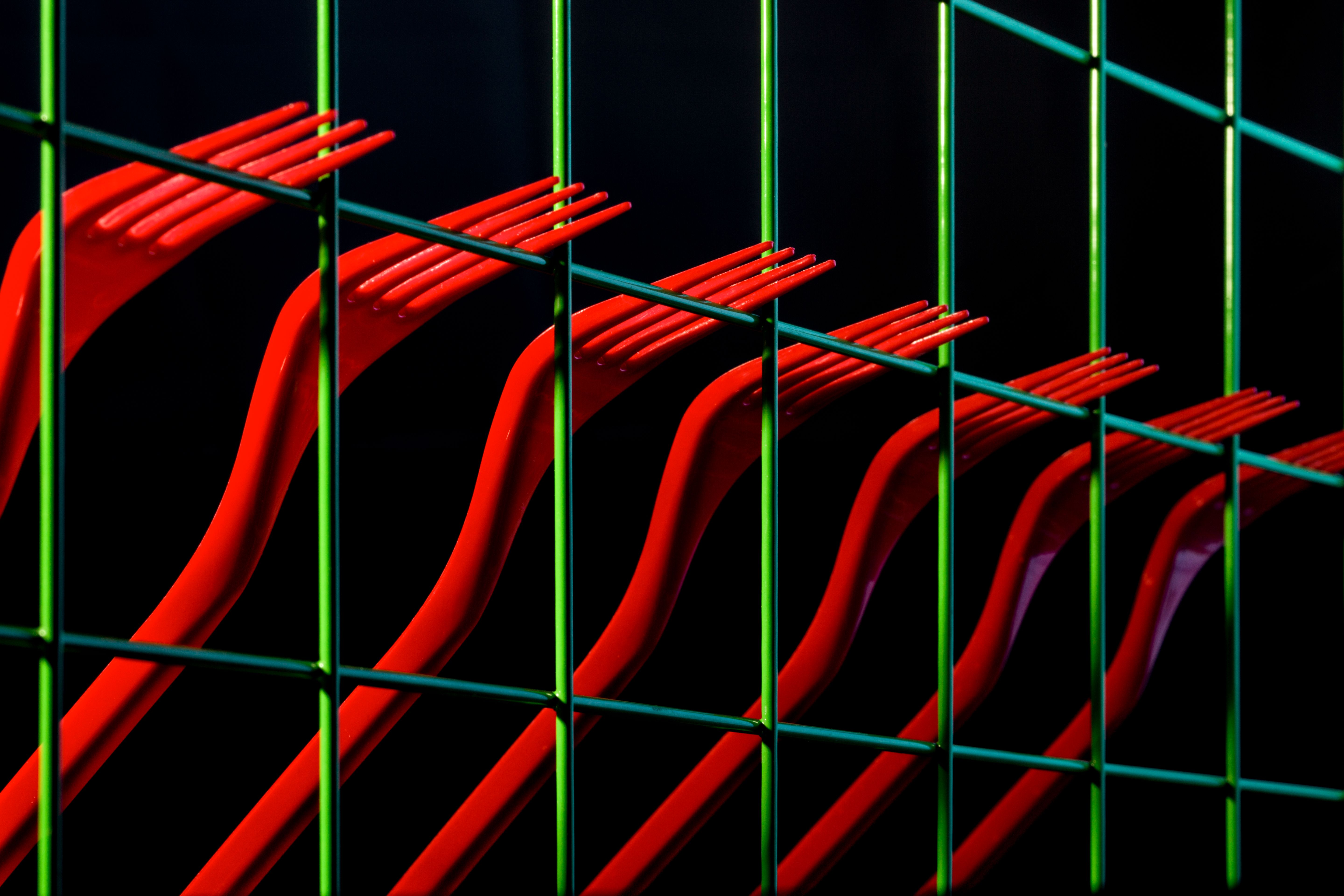 Vibrant red forks interwoven with a green grid on a dark background creating an artistic and abstract composition.