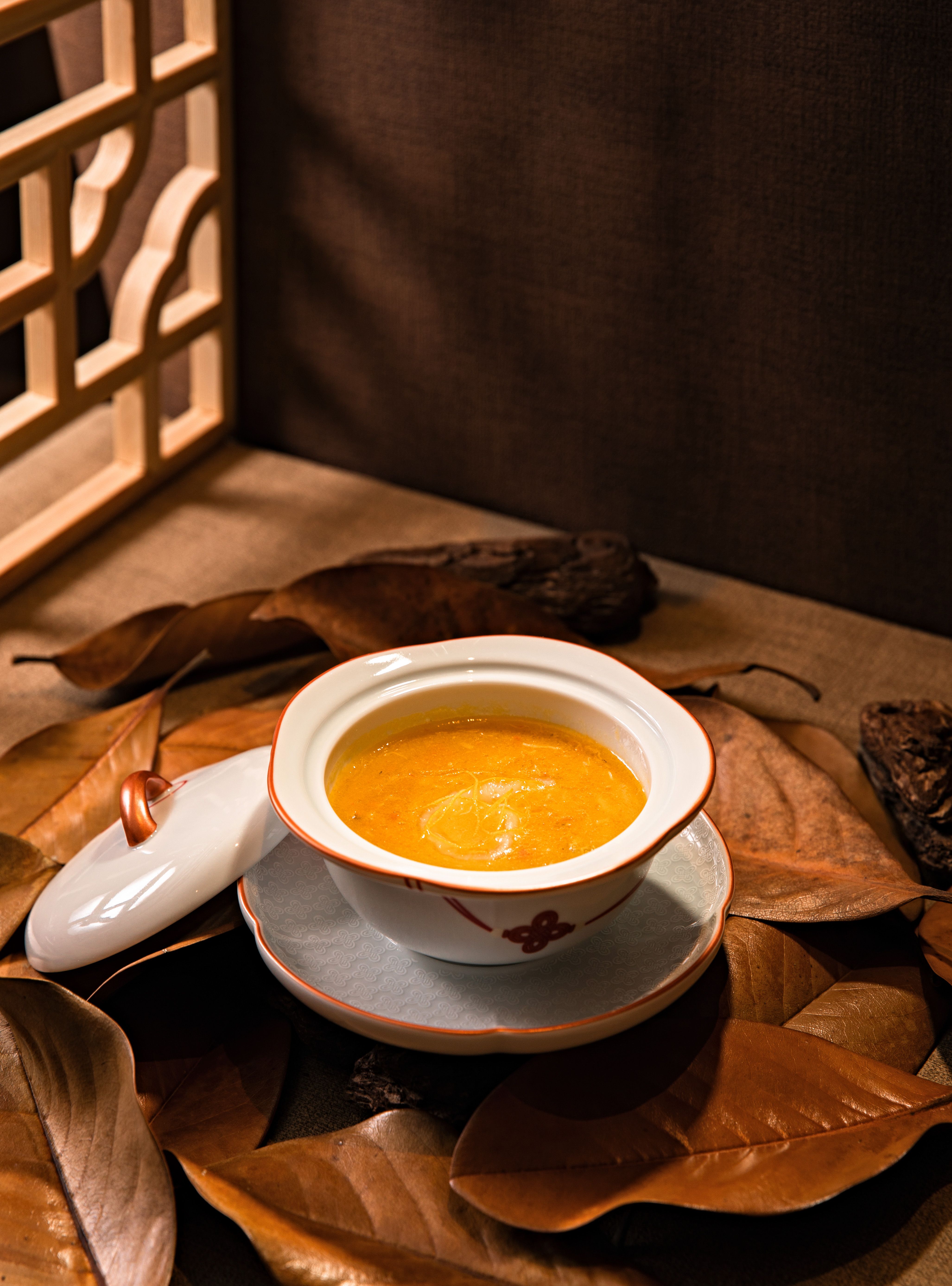 Cozy pumpkin soup in an elegant bowl, surrounded by autumn leaves, warm ambiance.