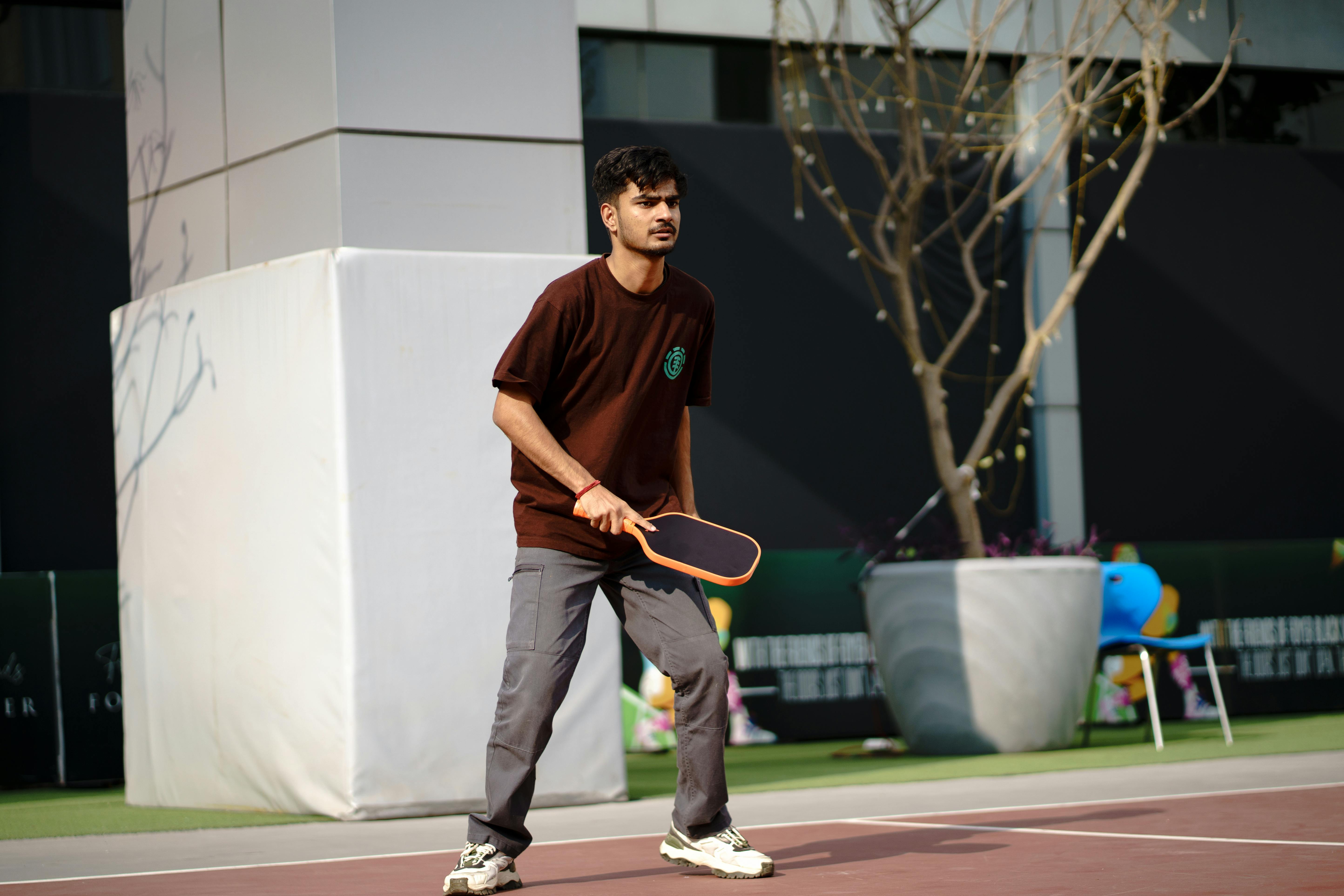 A young man actively playing pickleball on an outdoor court, showcasing concentration and skill.