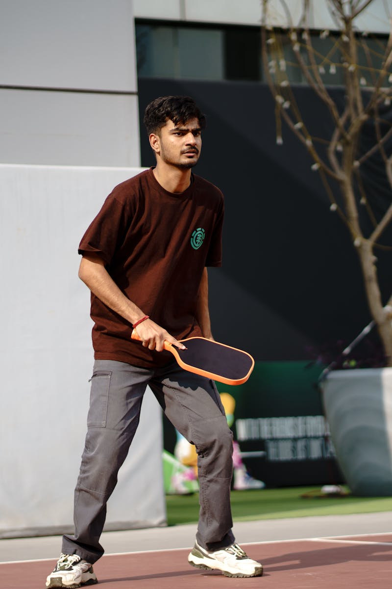 A young man actively playing pickleball on an outdoor court, showcasing concentration and skill.