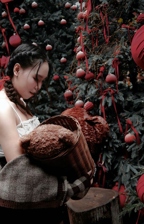 Free A woman holding a teddy bear in a basket stands by a beautifully decorated Christmas tree. Stock Photo