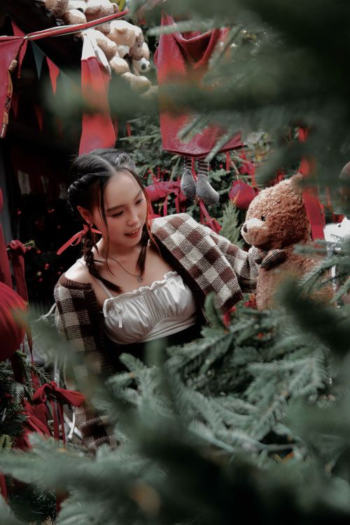 Free A woman admires a teddy bear amid festive Christmas decorations and trees. Stock Photo