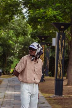 Man in fashionable attire with a headscarf, set in a green urban park background.