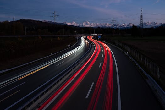 Night view of a highway in Bern with light trails from vehicles and Alps in the background.