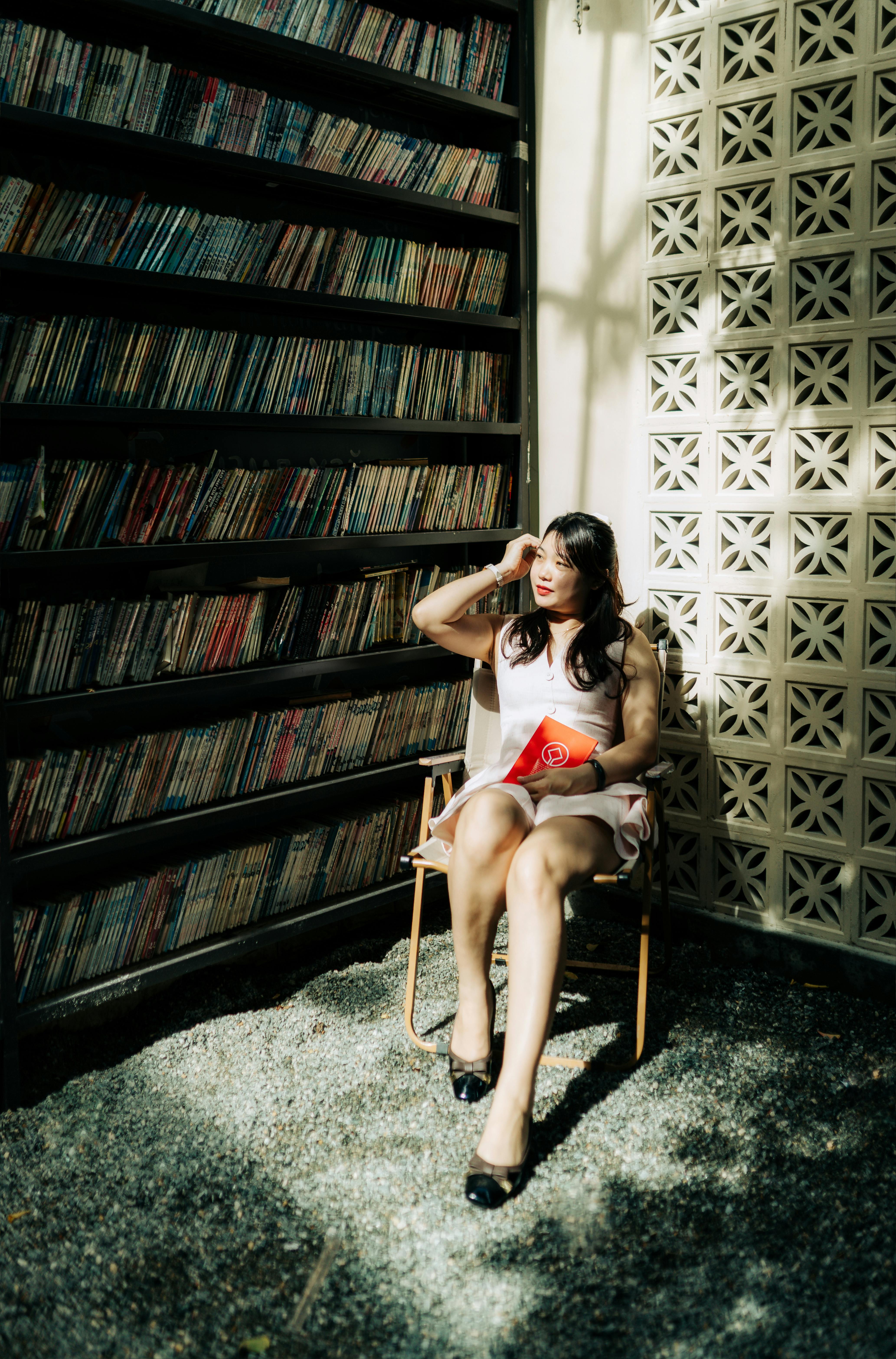 A woman sitting in a sunlit library corner, surrounded by bookshelves, exuding relaxation and contemplation.