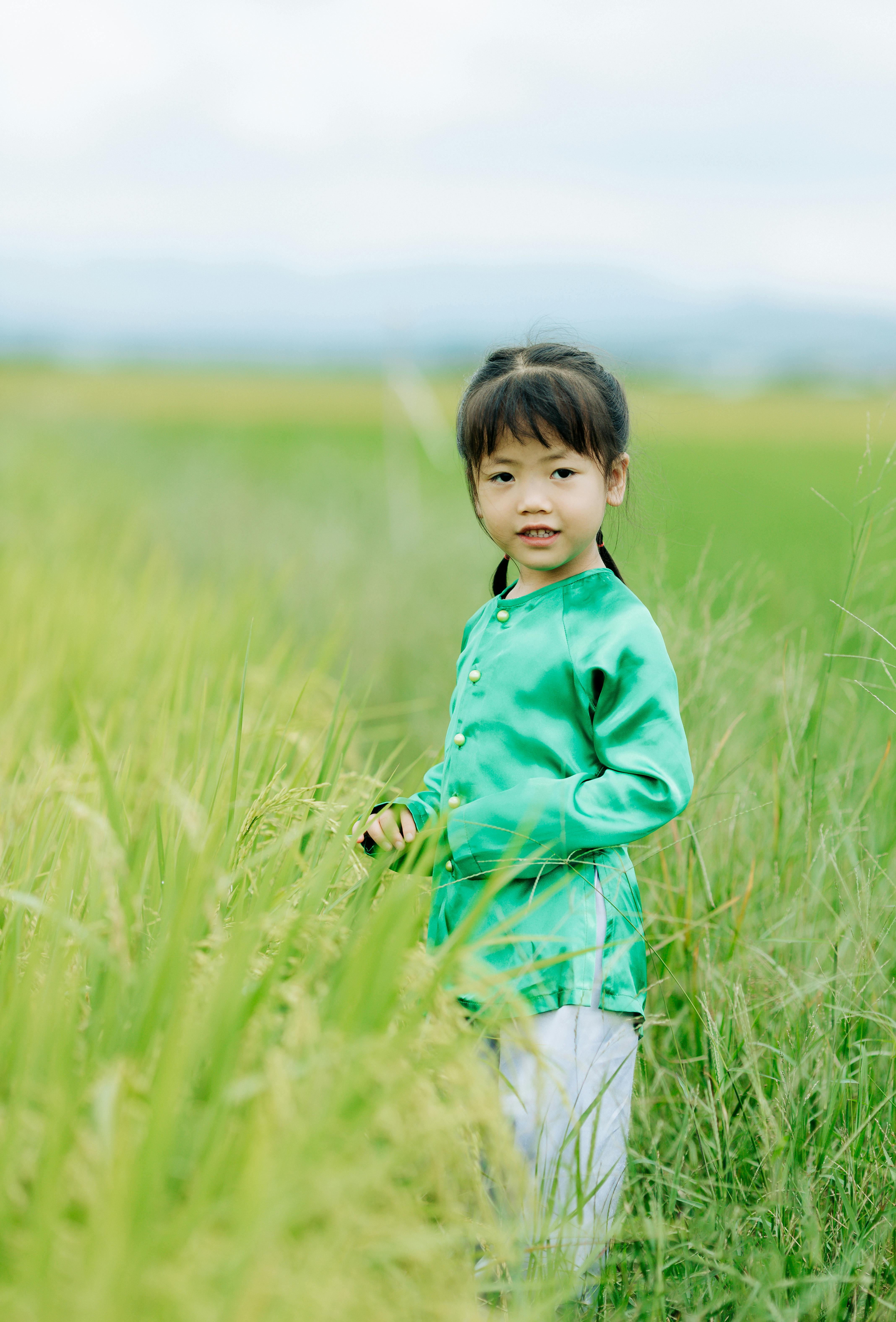 A young child in traditional green attire smiles amidst a lush rice field in Kon Tum, Vietnam.