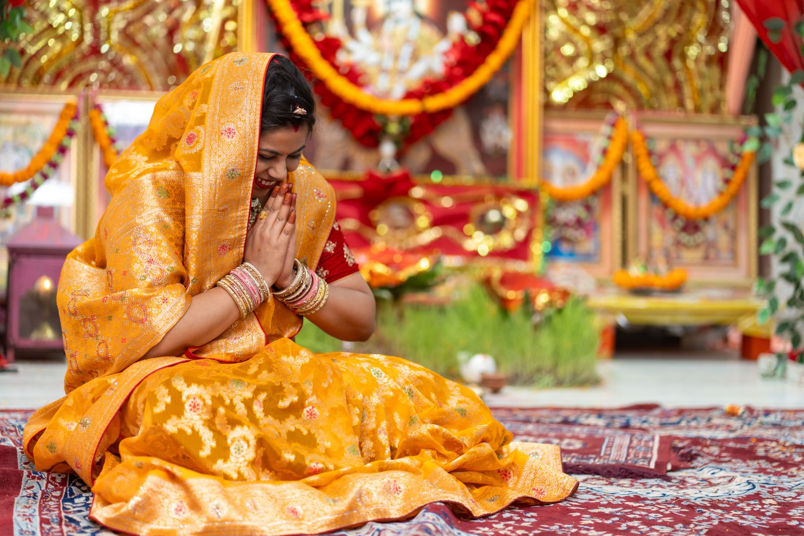 Woman in traditional yellow sari performing a devotional prayer ceremony, representing the practice of bhakti yoga