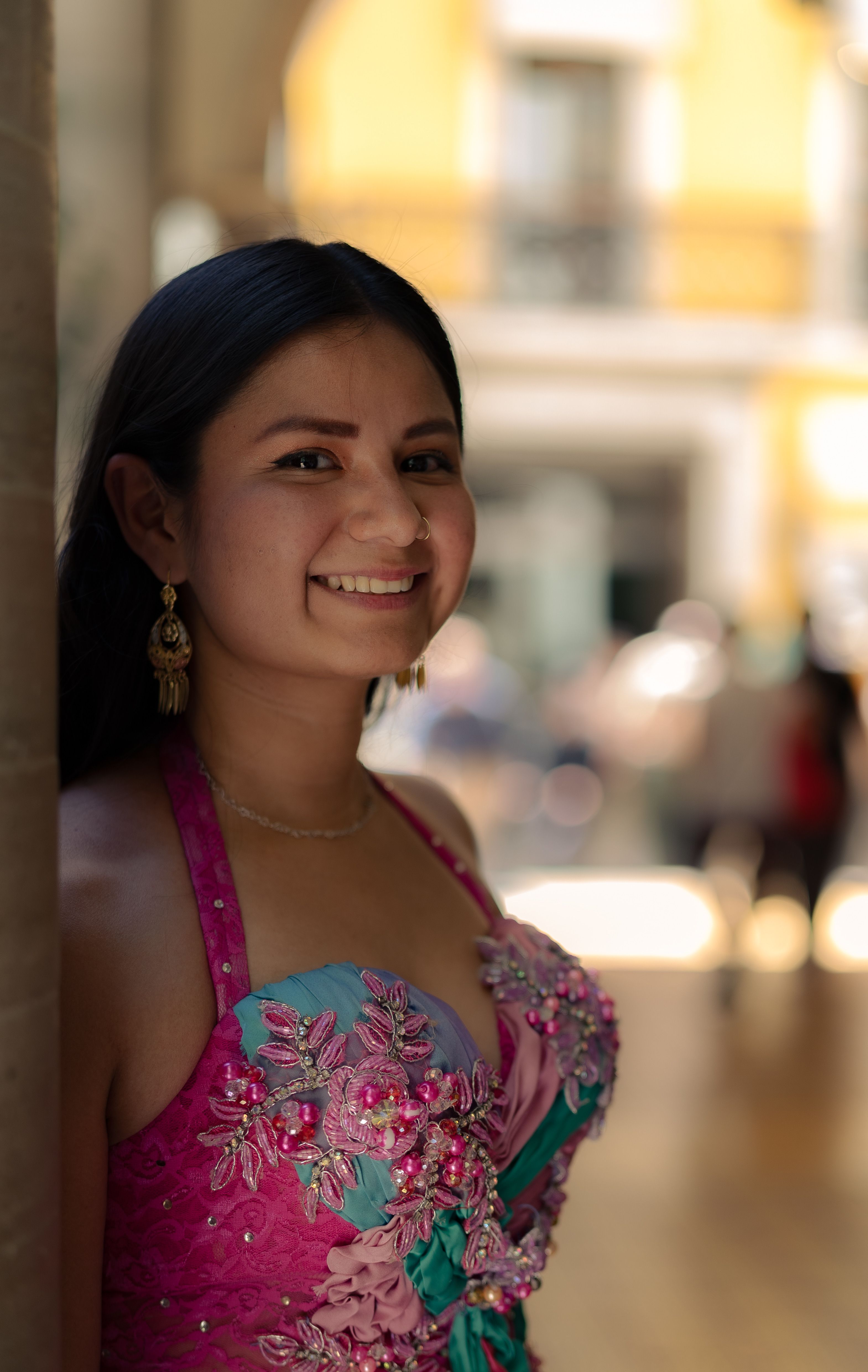 Smiling woman in colorful floral dress stands outdoors, exuding elegance and joy.