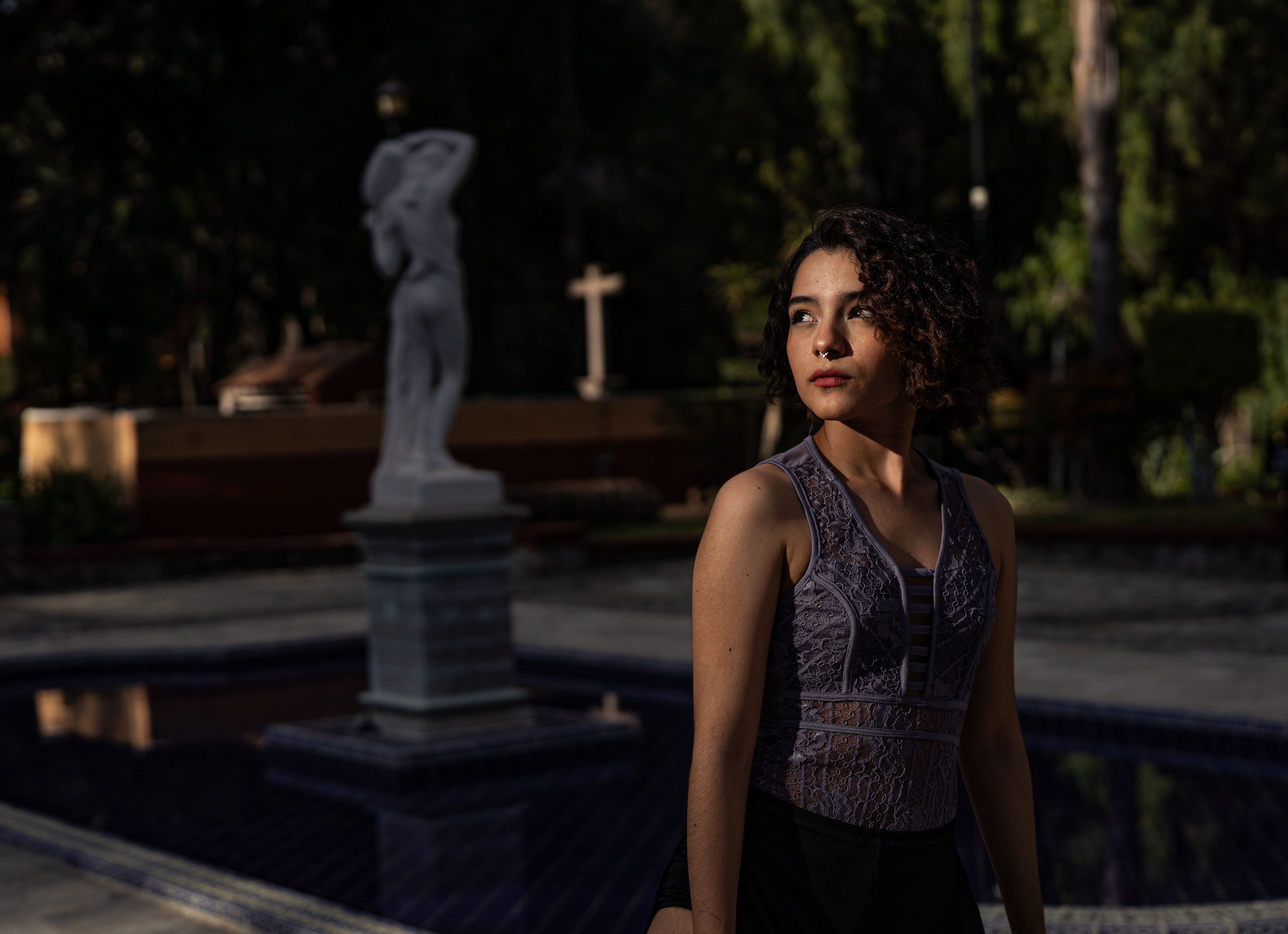 Portrait of a woman in a garden with statue at sunset, thoughtful and serene.