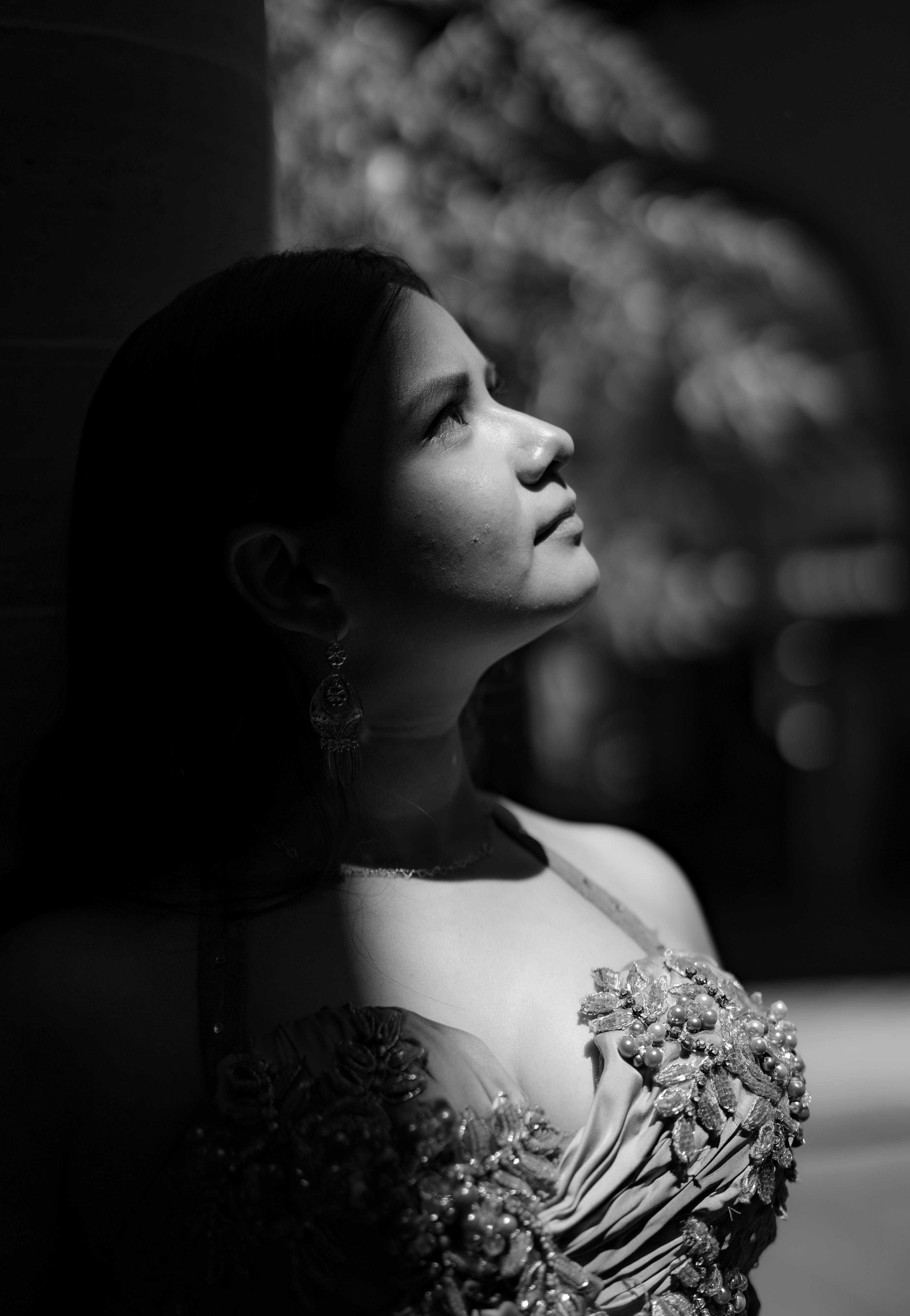 A woman in a decorative dress gazes upward, illuminated by striking light.