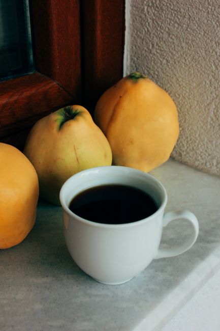Warm cup of coffee with fresh quince fruit on a cozy indoor windowsill setting.