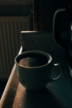 A warm cup of coffee basking in morning light on a kitchen counter, creating a cozy atmosphere.