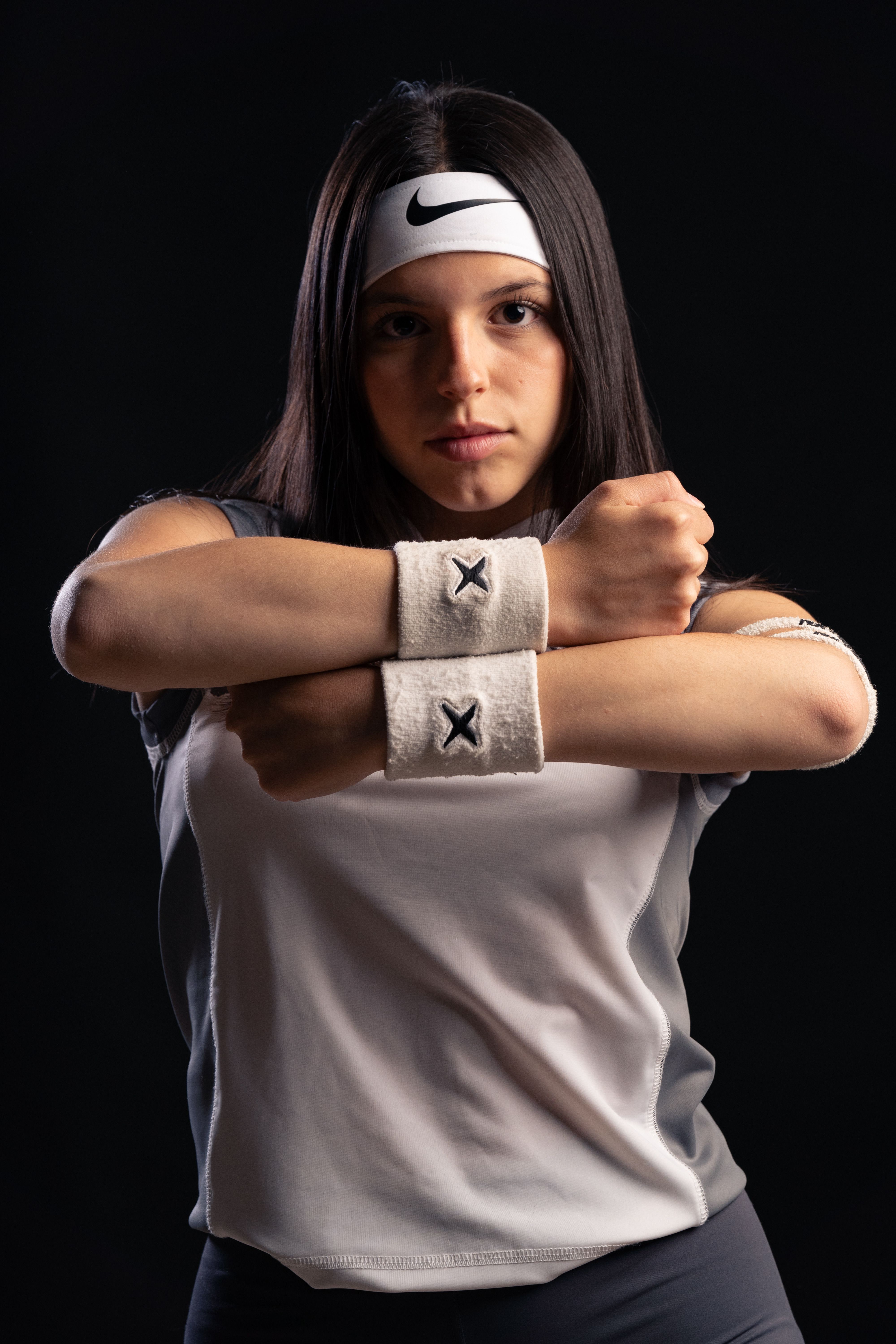 Confident young woman athlete posing in sports gear against dark background.