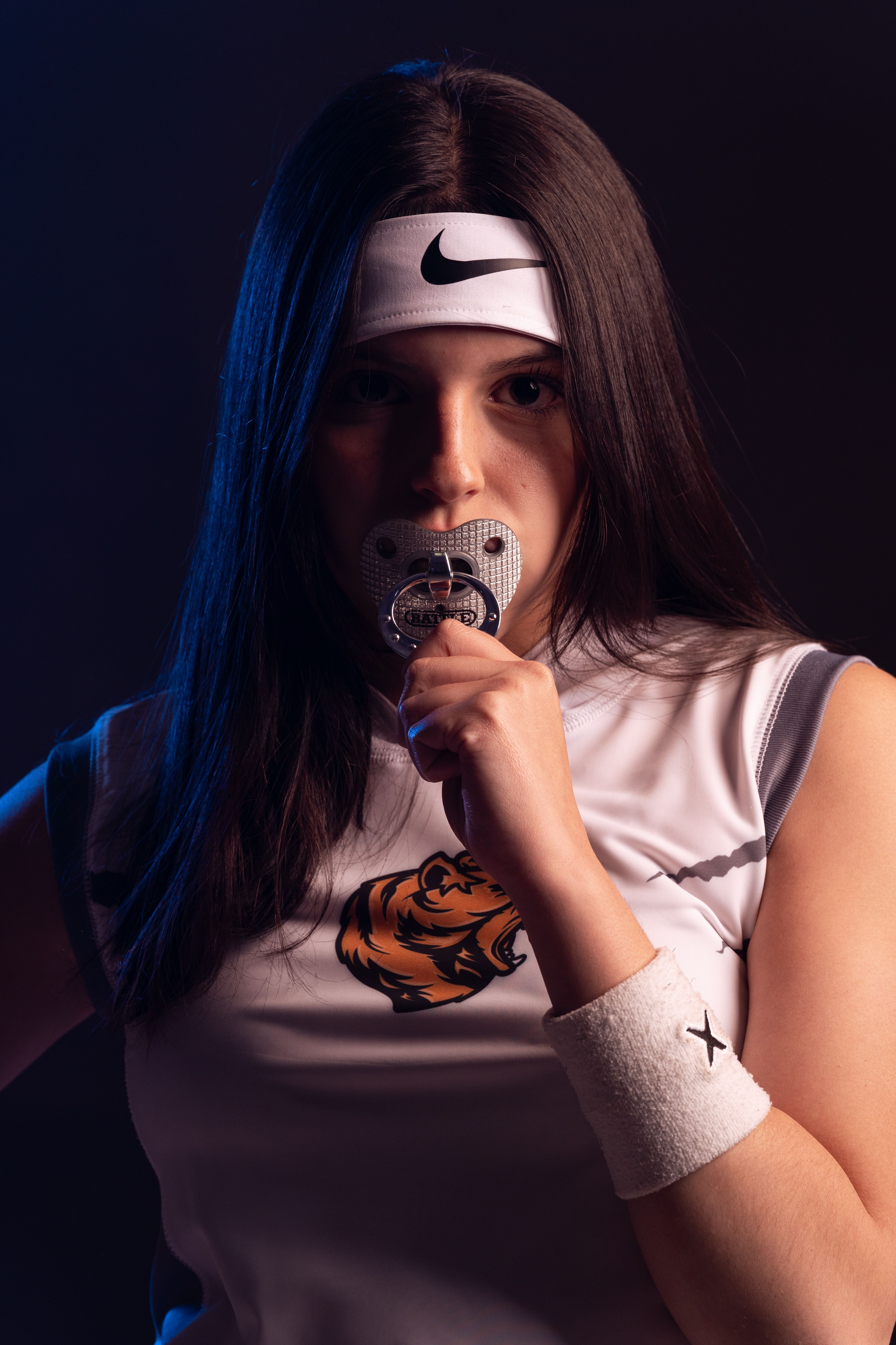 A dedicated female athlete in sports attire holding a medal, wearing a headband in dramatic lighting.