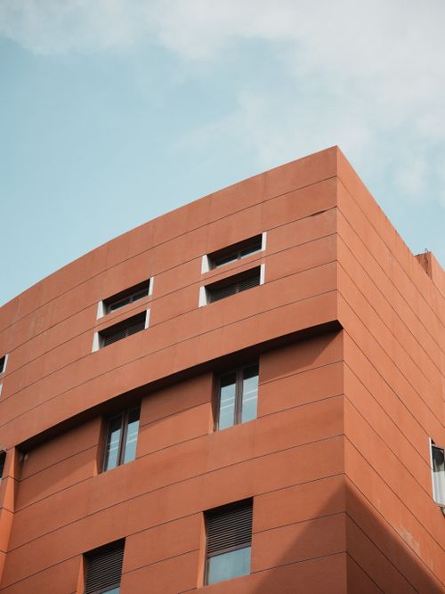 Free A modern orange building with large windows stands against a clear blue sky. Stock Photo
