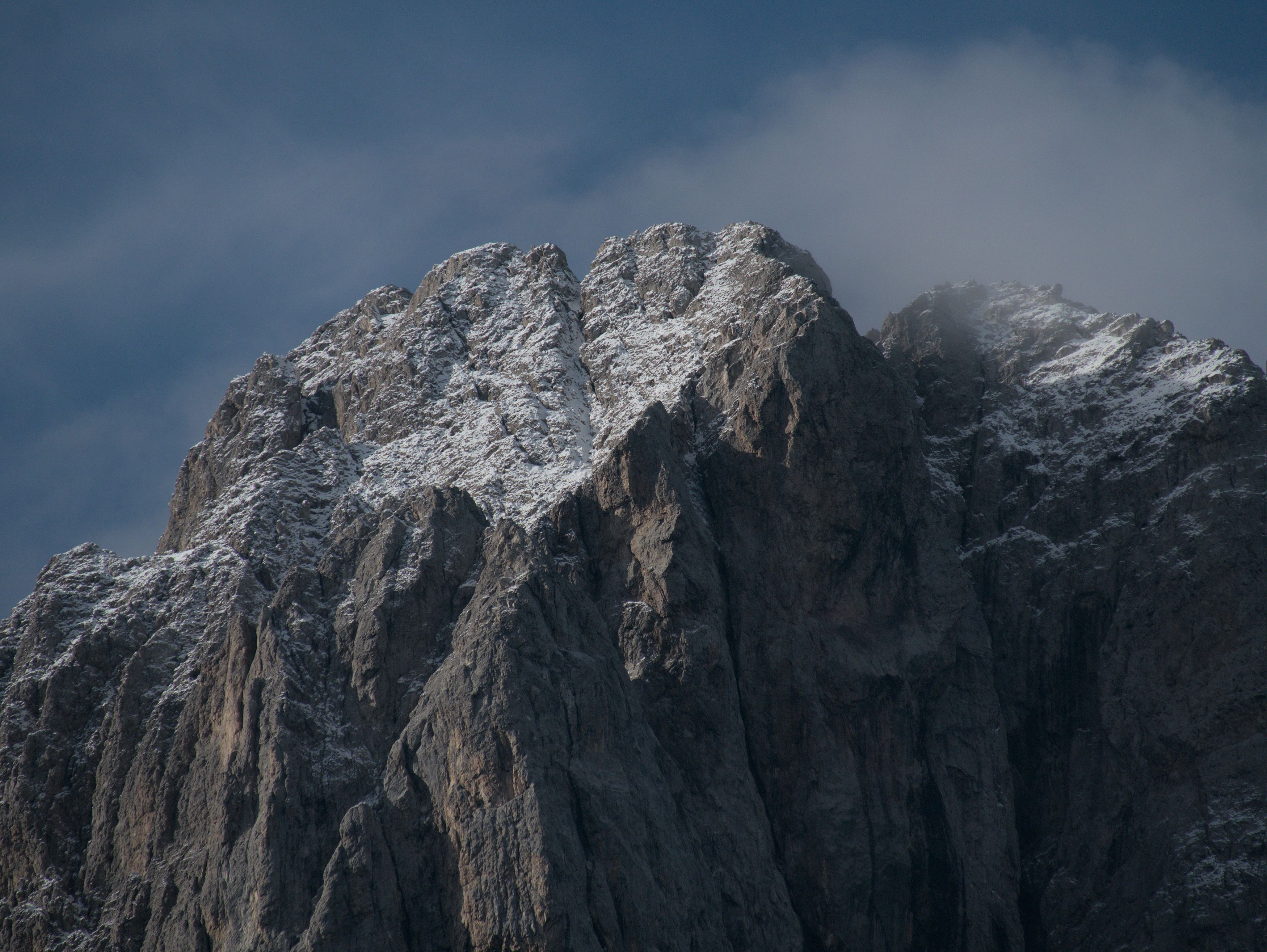 A majestic snow-dusted mountain peak under a clear blue sky in the Dolomites, Italy.
