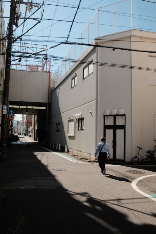Free A lone pedestrian walks along a shadowy urban street with overhead power lines and modern buildings. Stock Photo
