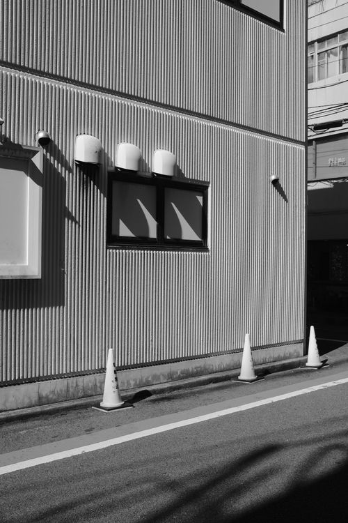 Free Black and white photo of an urban street corner with traffic cones and a corrugated metal building. Stock Photo