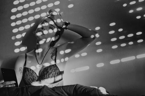 Artistic monochrome shot of a tattooed woman relaxing in lingerie with light patterns.