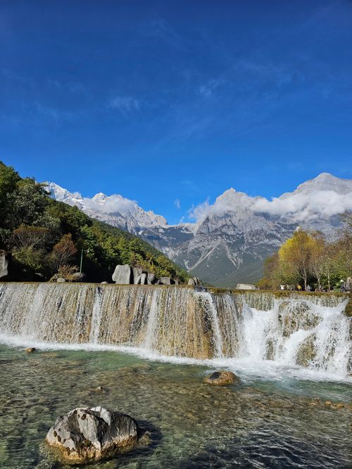 Free A picturesque waterfall cascading in front of snow-capped mountains on a clear sunny day. Stock Photo