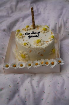 White cake adorned with daisies and a single candle, perfect for celebrations.