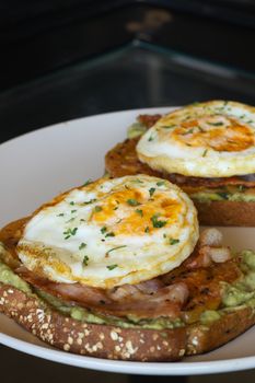 Mouthwatering avocado toast topped with fried eggs and crispy bacon for a gourmet breakfast.