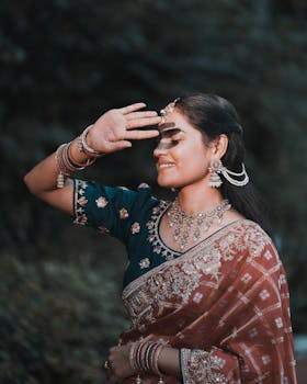 Beautiful Indian bride posing outdoors in traditional saree with intricate jewelry and henna designs.