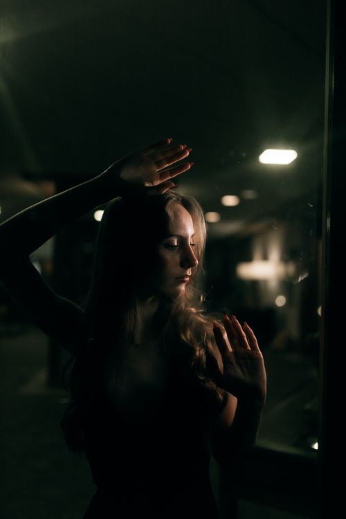 Free A dramatic, moody portrait of a woman in a dimly lit urban setting at night. Stock Photo