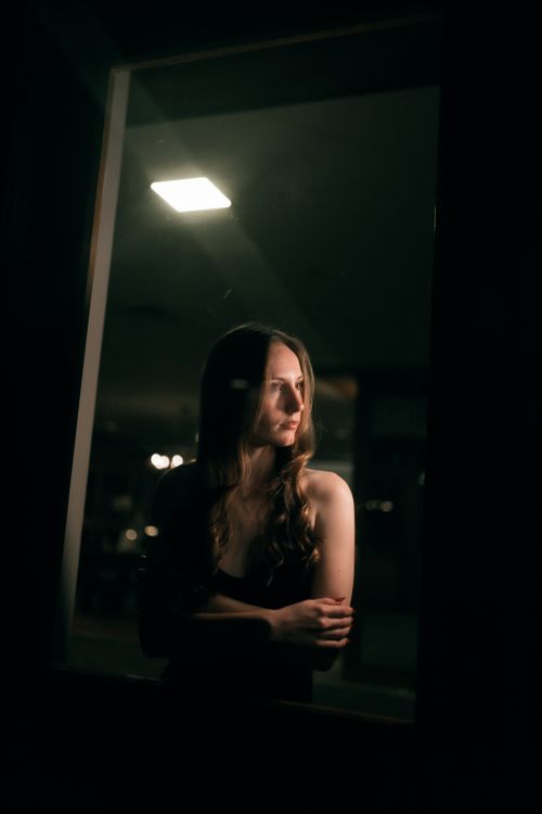 Free Contemplative woman looking through a window at night, ambient lighting. Stock Photo