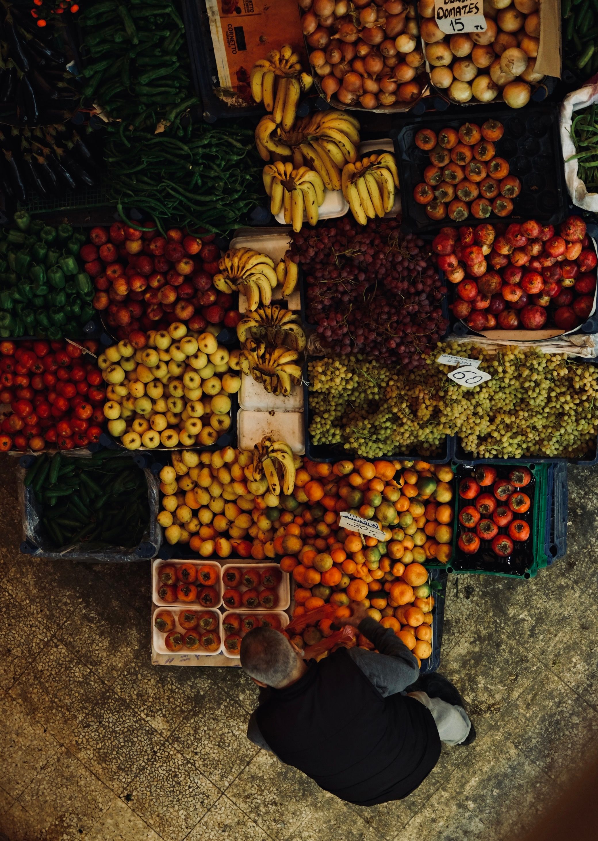 Aerial view of a colorful fruit market stand with a person browsing produce.